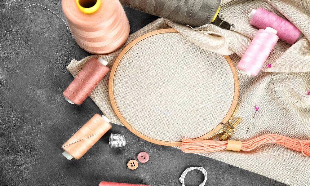A collection of embroidery accessories laying on a gray table. There are five spools of thread, a thimble, and a loom.