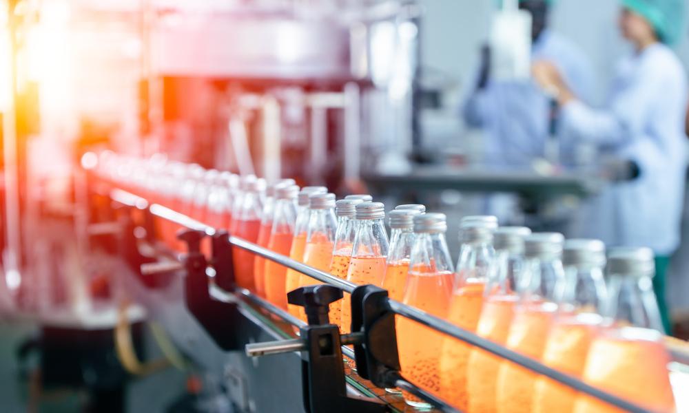 A conveyor belt feeding transporting plastic bottles with orange and red liquid inside through a factory.